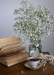 Still life with cup of tea. Simple composition photo with small white flowers and cup of black tea on a table. Beautiful morning picture. 