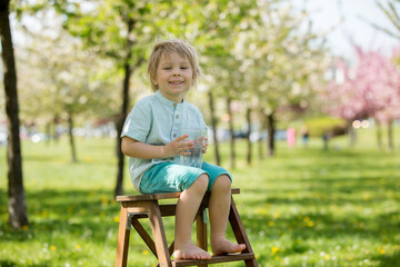 Beautiful blond child, boy, drinking water in the park on a hot day