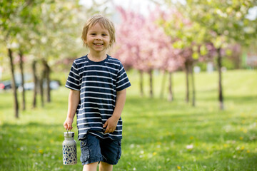 Beautiful blond child, boy, drinking water in the park on a hot day