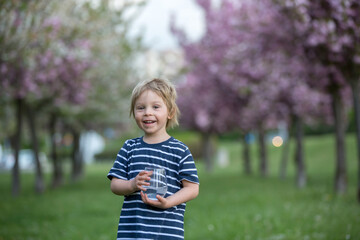 Beautiful blond child, boy, drinking water in the park on a hot day