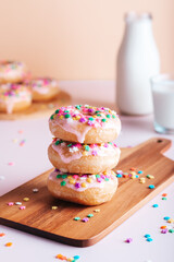 Stack of freshly made home cooked donuts with icing and sprinkles and milk bottle and glass in background