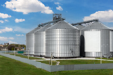 Scenic view of big modern steel agricultural grain granary silos cereal bin storage warehouse against blue sky. Agribusiness farmland rural industry silo landscape scene. Mill store farm facility