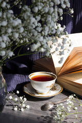 Still life with open book, glass vase with white gypsophila flowers, green pear on kitchen towel. Leisure time concept. Simple composition photo on blue background.