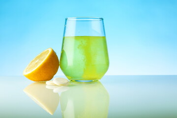 effervescent vitamin C tablet dissolves in water. a glass of water, effervescent tablet and citrus fruit on blue background. vitamin C concept