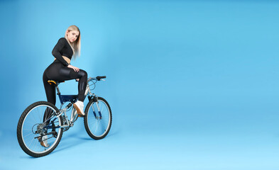 Fototapeta premium studio shot of a sportive woman sitting on a bicycle on blue background with copy space. beautiful young woman wearing sportswear posing with a bike in a photo studio