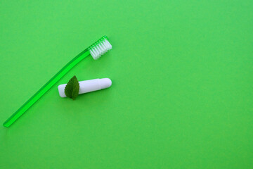 Toothbrush and a small tube of toothpaste with a mint leaf on a green background. Travel kit for brushing your teeth. 