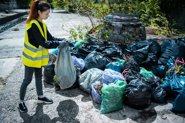 young female volunteer cleaning up park and standing by bunch of sgarbage bag