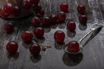 Washed ripe juicy red grapes with berries in water droplets and an antique spoon on a wooden table. Still life in a gloomy mood.
