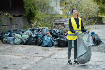 young female volunteer cleaning up park and standing by bunch of sgarbage bag
