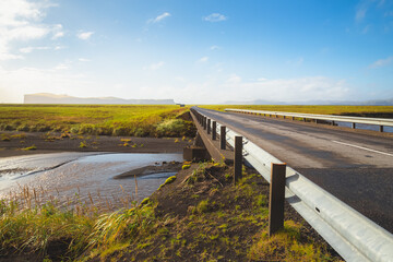 Fototapeta premium An empty paved road through scenic countryside landscape on a bright sunny day in Southern Iceland near Skeioflotur.