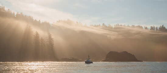 Atmospheric golden light sunbeams through morning mist and fog over an ocean fishing boat off the...