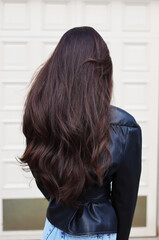 Long, thick, dark natural hair. Hairstyle. Loose strands lie in beautiful waves. Portrait of a Caucasian lady from the back