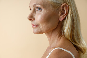 Close up portrait of mature blonde woman in white underwear looking away, posing isolated over beige background