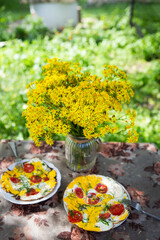 Delicious and healthy breakfast outdoors. Omelet with tomatoes and herbs. Summer cottage, rest, fresh air. A bouquet of flowers on the table.