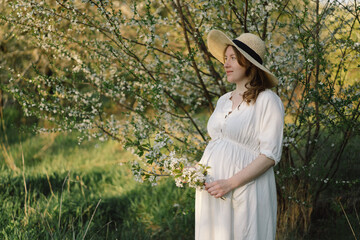 Spring portrait of a pregnant woman. A beautiful young pregnant woman in a white dress walks in the spring garden.