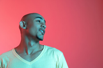 African-american young man's portrait on red studio background in neon. Concept of human emotions, facial expression, youth, sales, ad.