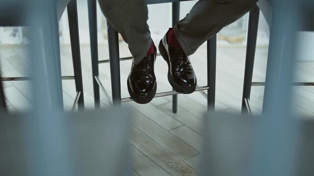 Lonely waiting man keeping distance, nervously moves feet in shoes while sitting on bar stool 