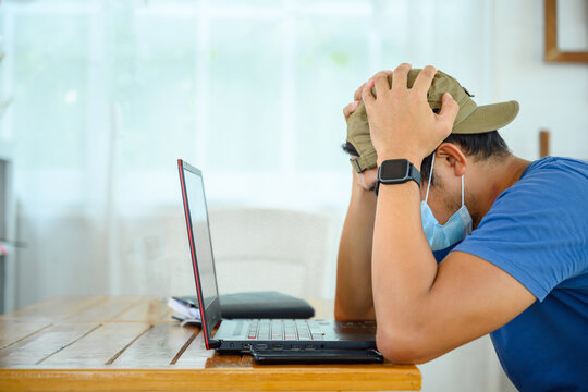 Young Asian Male Freelance Wear a mask The quarantine preventing the spread of COVID 19 is stressful and frustrated by reading email news from a laptop computer. Depressed male freelance