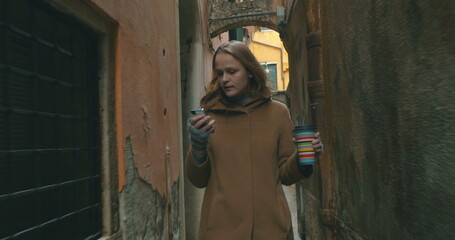 Woman with phone and coffee walking in Venice