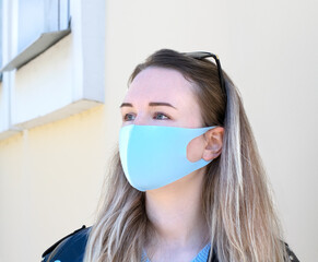 Young woman with blond hair is wearing blue reusable face mask 