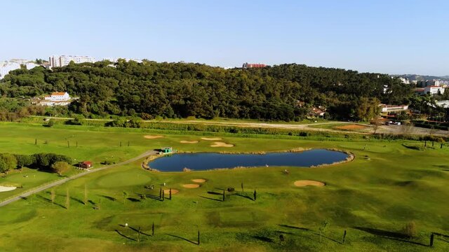 Aerial view over the Golf Course at the National sports center of Jamor, in sunny, Oeiras, Lisbon, Portugal - reverse, drone shot