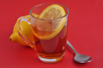 Mug de thé au citron à côté d'un citron et d'une cuillère en gros plan sur fond rouge