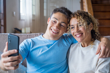 Smiling middle-aged 40s mother rest with grown-up son using smartphone together, happy young man enjoy family weekend with mom browsing wireless Internet on cellphone, have fun at home
