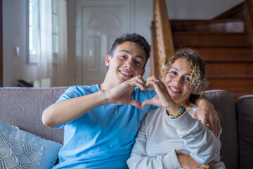 Portrait of couple of mom and son together a home making a heart love shape with their fingers and...