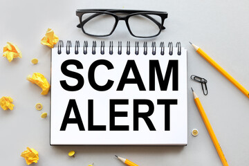 SCAM ALERT. text on notepad near torn stickers on gray background.