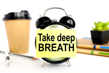 Take a Deep Breathe. there is a sticker on the alarm clock. against the background of a paper cup with coffee and plants in a pot. alarm clock on white background