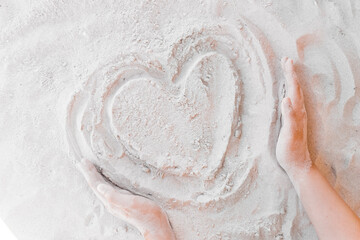 The hand of a young girl draws a heart on the white beach sand close-up. Symbol or sign of love concept