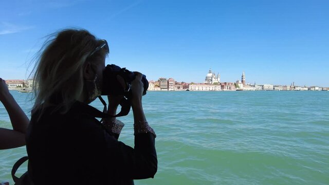 photographer girl taking pictures in Venetian lagoon at San Marco bell tower and Doge Palace with Venice Saint Mark Basilica. Giudecca canal by cruise boat trip in lagoon of Venice italian city