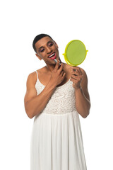 african american transvestite man in sundress applying lipstick while looking in mirror isolated on...