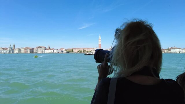 girl photographing San Marco bell tower and San Marco square in Venice with Saint Mark Basilica of the famous Venetian city of Italy. Giudecca canal by cruise boat trip in Venetian lagoon.