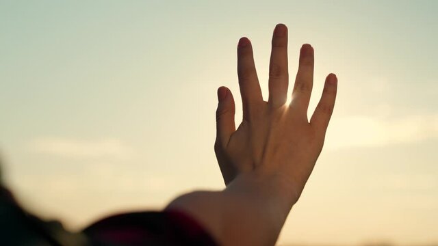 Hand of happy girl reaches for sun. Sunset between hands of girl. Girl dreamily stretches out her hand to sun, rays of sun shine through her fingers. Hand of childs dream to sun. Happy family concept