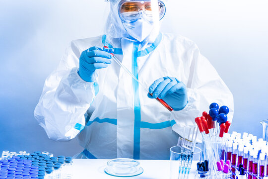 Medical laboratory with equipment and Microbiology scientist wearing ppe scrubs, face shield mask, works with Petri dishes pipette, various tissue and blood samples. Develop vaccine, drugs research.