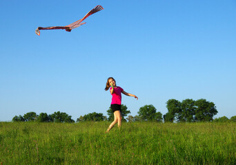 Girl playing with flying kite on meadow.