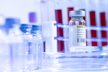 Glass bottle vial and syringe with Covid-19 Coronavirus vaccine in a research medical facility lab. Ampoules with cure on the medical worker laboratory table. Sars-cov-2 pandemic concept.