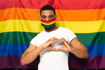african american man wearing rainbow colors medical mask and showing heart sign on background of...