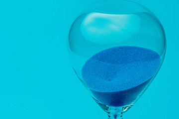 Hourglass with blue sand on blue background