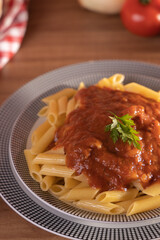 macarrão pene com molho de tomate sobre um prato fundo e mesa amadeirada em plano de fundo 