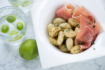 Italian gnocchi with basil pesto sauce and prosciutto ham served in a white plate, closeup, elevated view