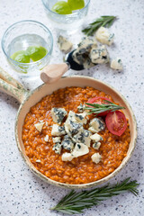 Risotto with sun dried tomato pesto and gorgonzola in a serving pan, vertical shot on a beige stone background