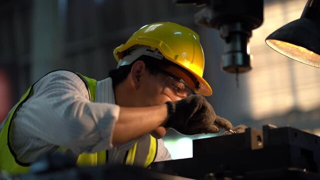 asian worker wearing helmet and safety glasses working  with machine in factory . industrial engineer operating plant drilling  machine