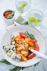 Potato gnocchi with sun dried tomato pesto, cherry tomatoes and gorgonzola, vertical shot on a light-grey marble background