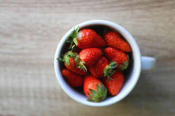 Mug filled with fresh strawberries on wooden table. Flat lay.