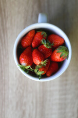 Mug filled with fresh strawberries on wooden table. Flat lay.