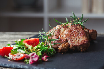 Grilled beef steaks on black stone slate. Tasty juicy grilled steak and salad with tomatoes. Main course beef dinner.