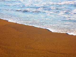 Wellen am Strand mit rotbraunem Sand