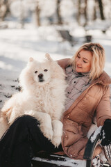 Pretty young woman walking and playing with samoyed dog on snowy winter morning.